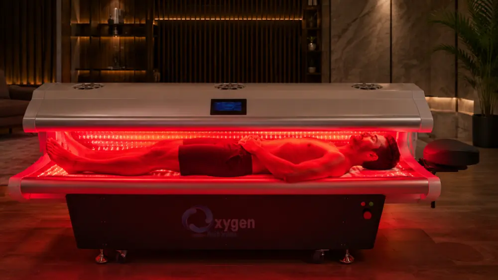 Man lying inside the open red light therapy bed in a luxury dark room bathed in red light
