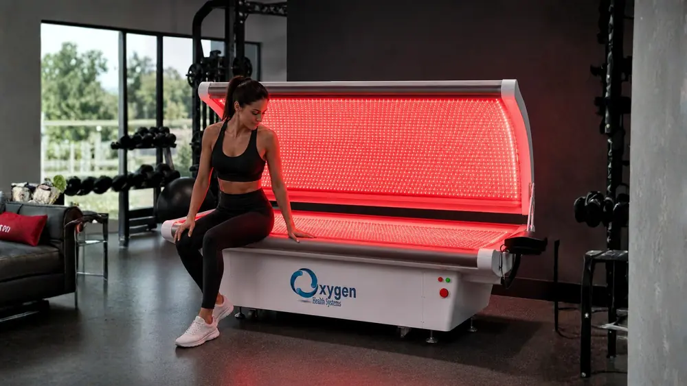 Athletic woman sitting on the edge of the open red light therapy bed in a gym setting