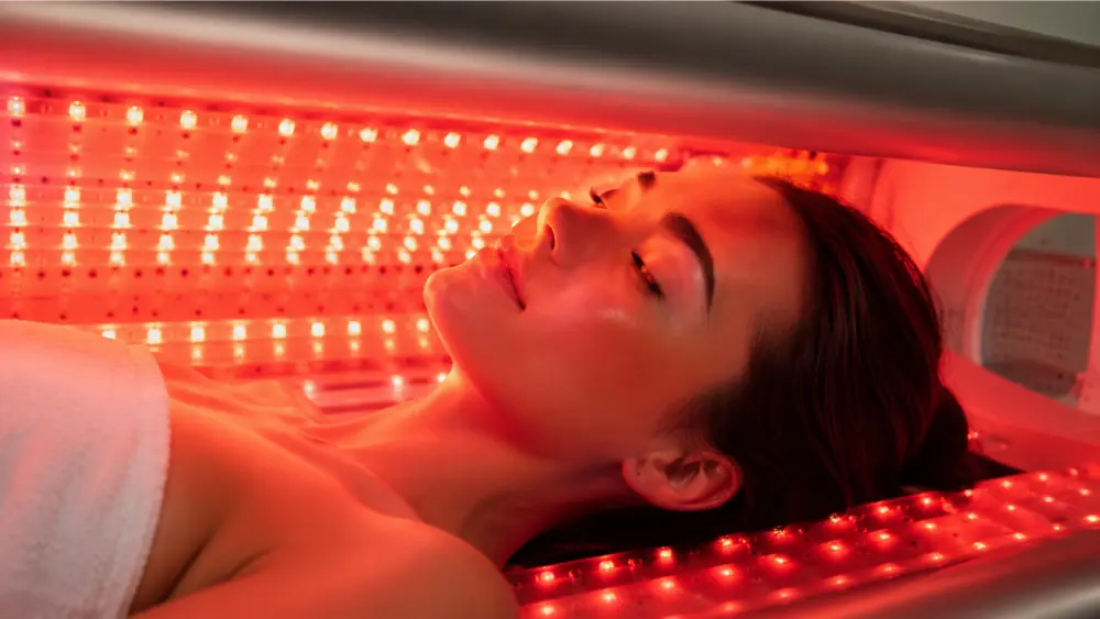 Close-up of a woman with eyes closed in the therapy bed, face illuminated by warm red LED light
